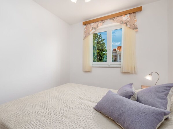 A bedroom with a bed, pillows, a nightstand, a lamp, and a window with curtains.