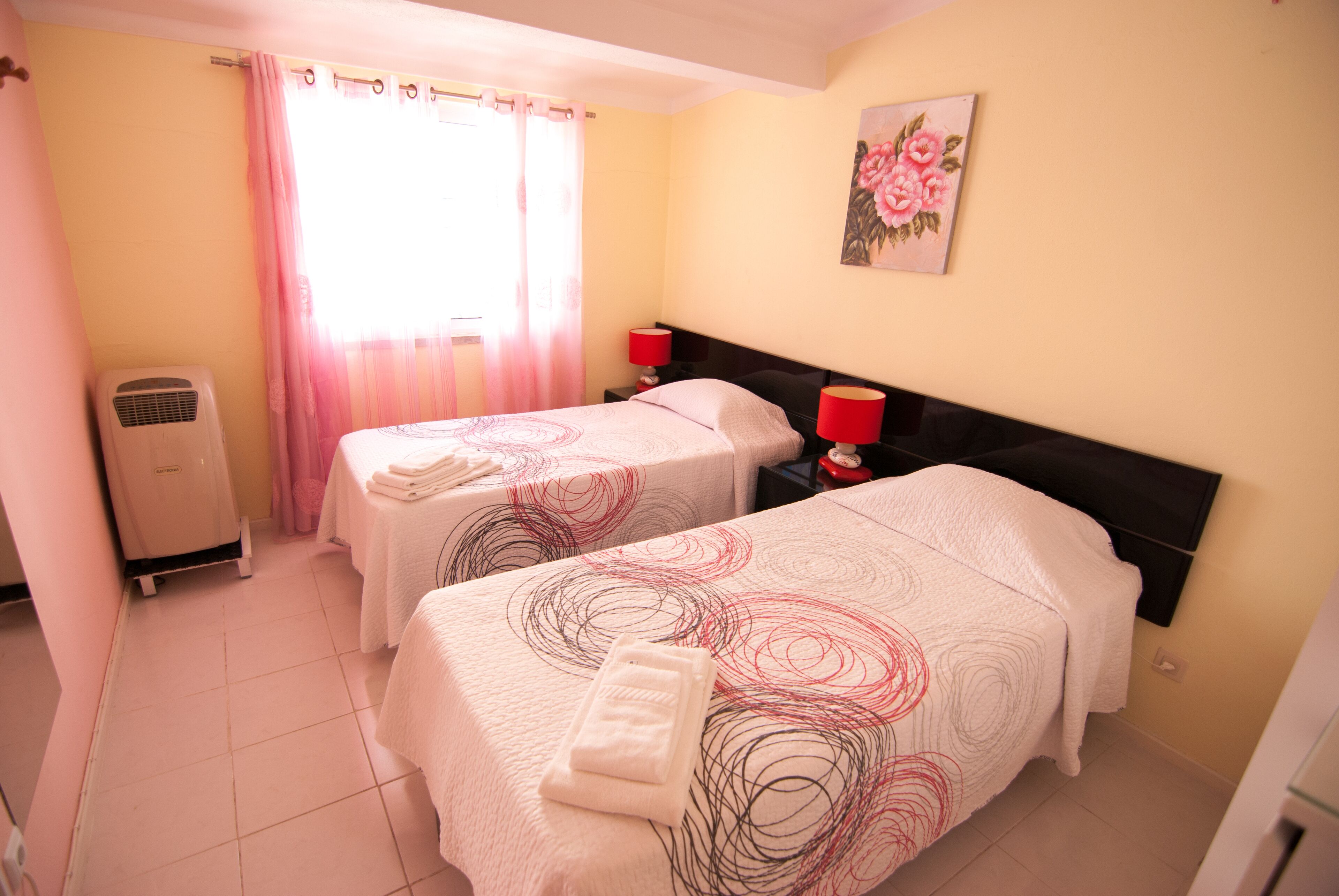 Une chambre d’hôtel avec deux lits, un radiateur, une fenêtre avec des rideaux et un tableau au mur.