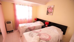 Une chambre d’hôtel avec deux lits, un radiateur, une fenêtre avec des rideaux et un tableau au mur.