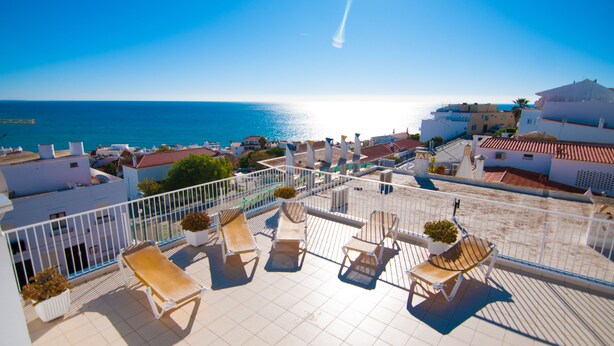 Une terrasse sur le toit, dotée de chaises longues et de plantes en pot, offrant une vue sur une ville côtière et la mer.