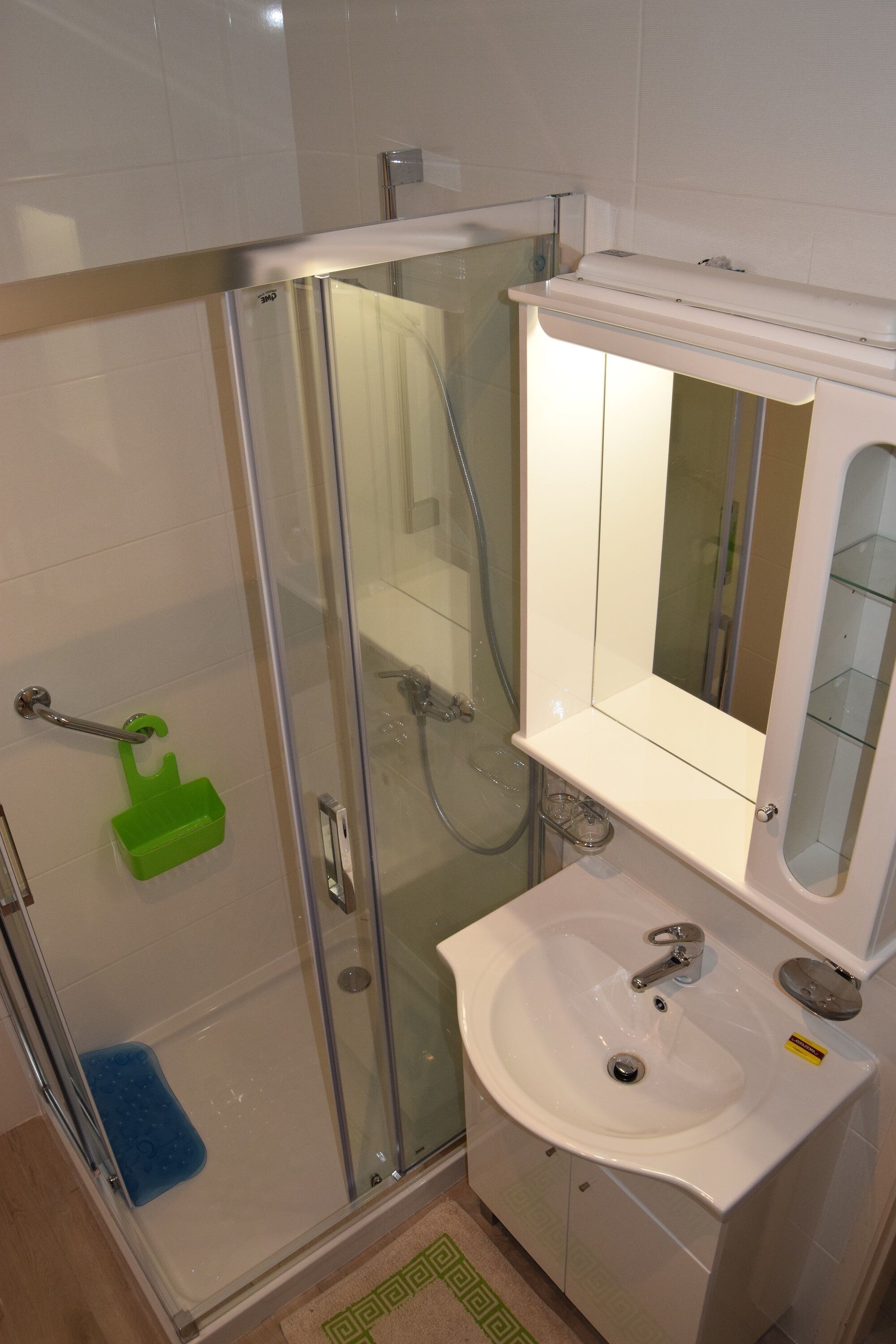 Un bagno con doccia vetro, un lavandino bianco con specchio sopra e un portasapone verde.