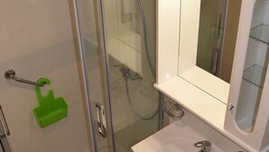 Une salle de bain avec une douche à parois de verre, un lavabo blanc avec un miroir au-dessus, et un porte-savon vert.