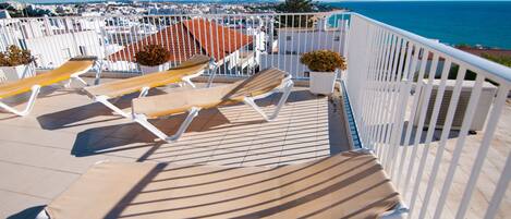 Een balkon met lounge stoelen en potplanten, met uitzicht op een kustplaats.