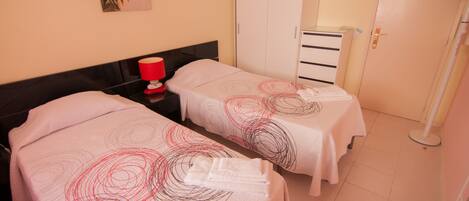 A hotel room with two beds, a wardrobe, a bedside table with a lamp, and a painting on the wall.