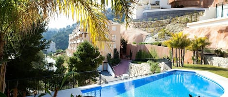 Una piscina de borde curvo, rodeada de vegetación y un muro de piedra.