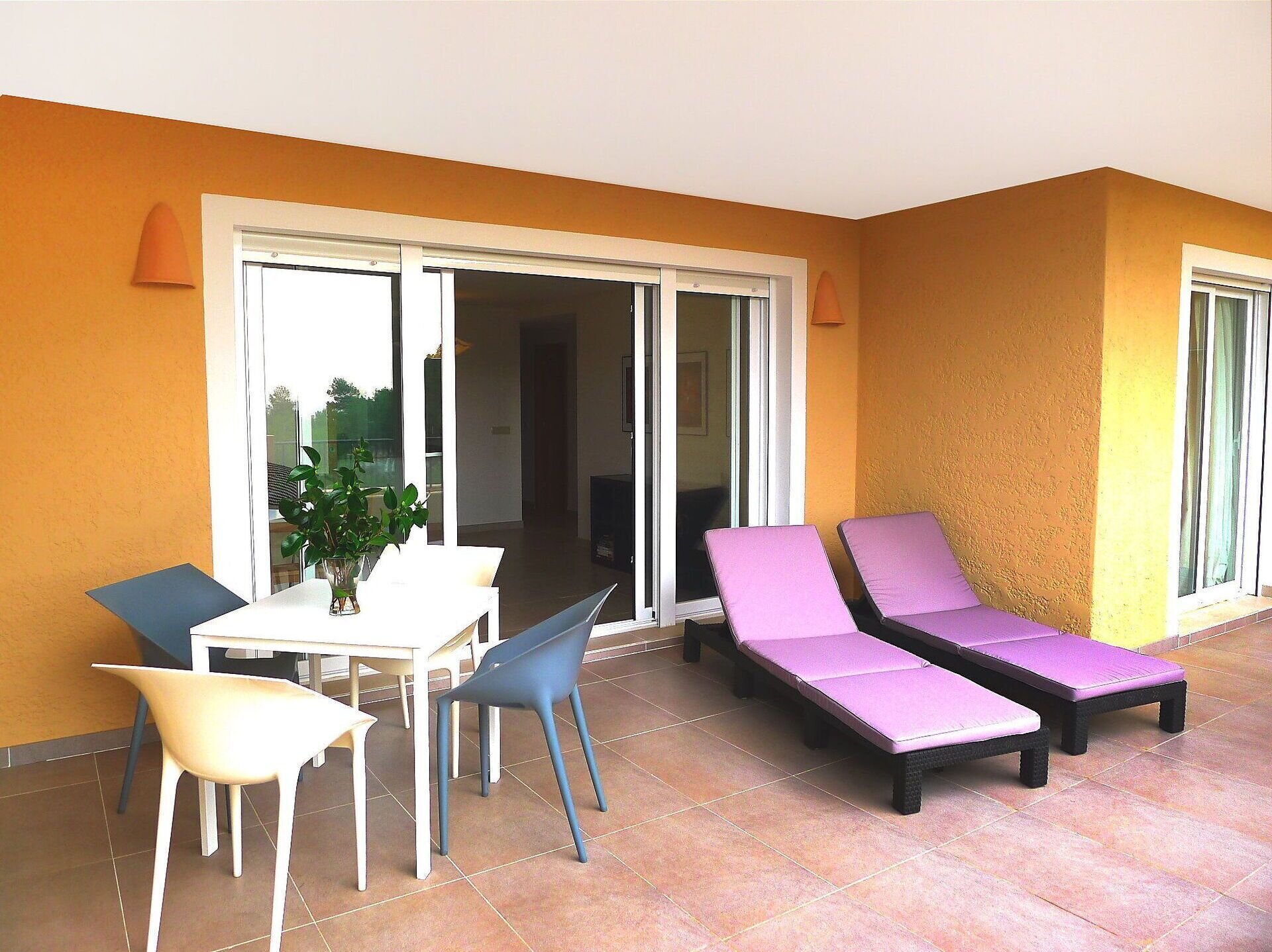 Un patio iluminado por el sol con una mesa, sillas, una planta en maceta y dos sillones.