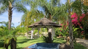 Un bain à remous dans un jardin agrémenté d’un belvédère, entouré d’une végétation luxuriante et de plantes en fleurs.