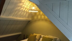 A cozy attic bedroom with a sloped ceiling, a bed with green and patterned pillows, and a hanging light fixture. - Authentic private cottage, beach a 15-minute walk 😍! (Vrouwenpolder)
