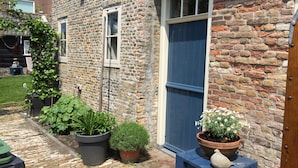 A brick building with a large window and a door. There are potted plants and a small table with a decorative item on it. - Authentic private cottage, beach a 15-minute walk 😍! (Vrouwenpolder)
