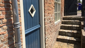 A brick building with a blue door, a window, and a set of stone steps leading to a gate. - Authentic private cottage, beach a 15-minute walk 😍! (Vrouwenpolder)