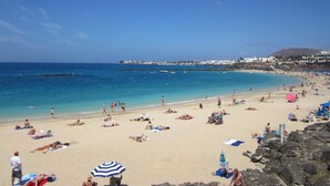 A beach with people sunbathing and swimming, clear blue water, and buildings in the background. - Fantastic villa with completely private pool, with high wall. Free wifi (Playa blanca)