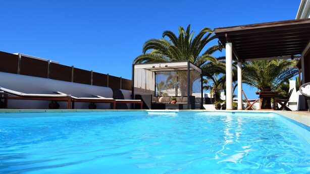 A clear blue pool with lounge chairs and a covered seating area, surrounded by palm trees. - Fantastic villa with completely private pool, with high wall. Free wifi (Playa blanca)