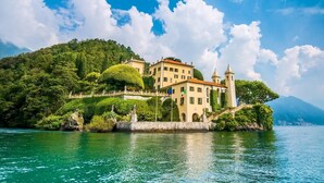 Un bâtiment historique doté d’une tour, situé sur une colline verdoyante, au bord d’un lac aux eaux d’un bleu limpide.