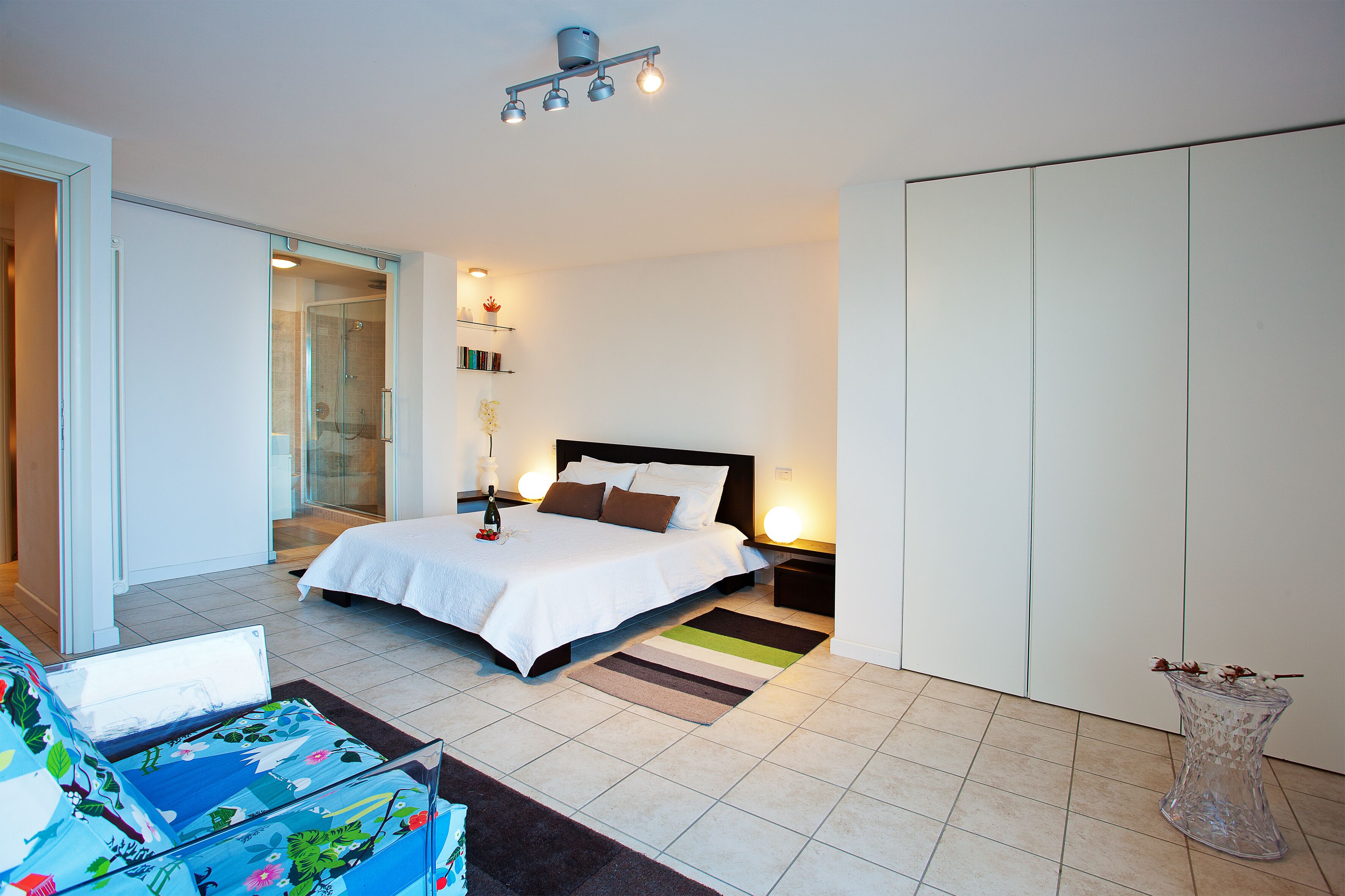 A modern bedroom with a bed, bedside tables, a glass coffee table, and a shower area.