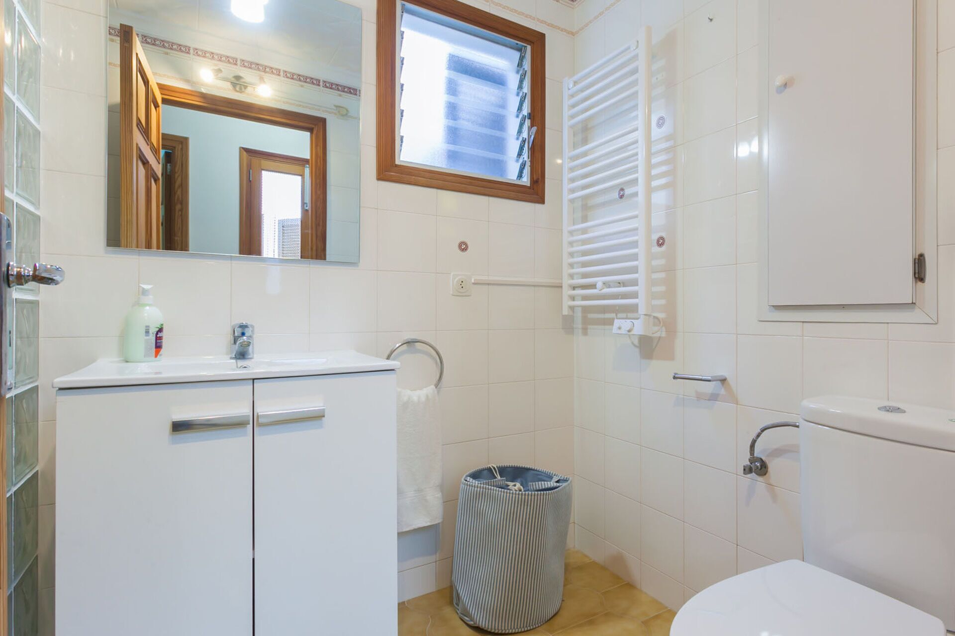 A bathroom with a toilet, sink, mirror, and window.