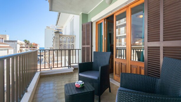 Un balcon agrémenté de meubles en osier, d’une petite table et offrant une vue sur la mer et les bâtiments.