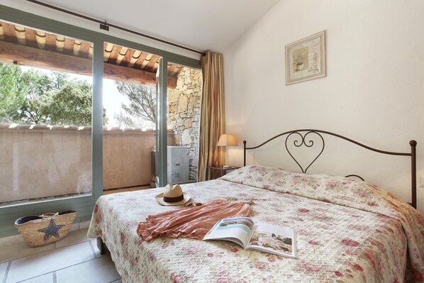A bedroom with a bed, a window, a wall-mounted picture, and a bedside table with a lamp.