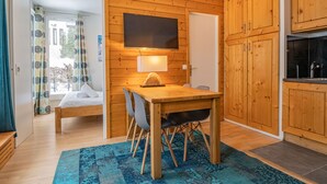 Ein gemütliches Zimmer mit einer Holzwand, einem Bett, einem Tisch mit Stühlen und einem darüber montierten Fernseher.
