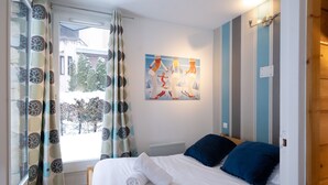 Ein Schlafzimmer mit Bett, einem Fenster mit Vorhängen, einem Bild an der Wand und einer Tür.