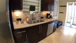 A modern kitchen with dark cabinetry, a granite countertop, a double sink, and a coffee maker. - 3BR Home wRooftop by Ideal Experience VR (Fort Lauderdale)