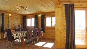 A wooden interior with a dining table and chairs, large windows with curtains, and a door leading outside. - Chalet - Montgellafrey (Montgellafrey)