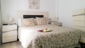 Une chambre à coucher bien rangée, avec un lit, deux tables de chevet, une œuvre d’art accrochée au mur et un plateau avec des fleurs posé sur le lit.
