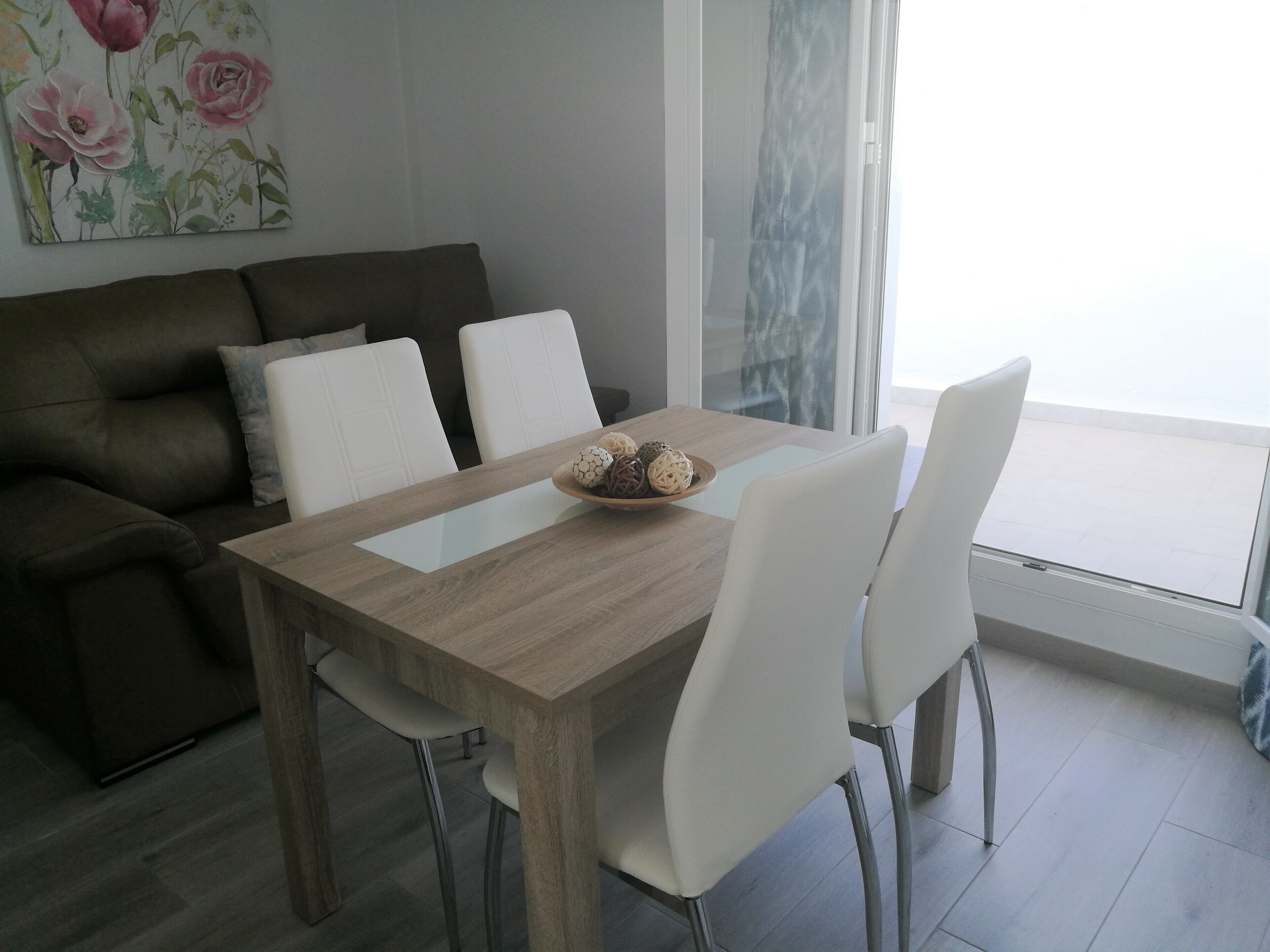 Et moderne spiseområde med et træbord, hvide stole og en sofa.
