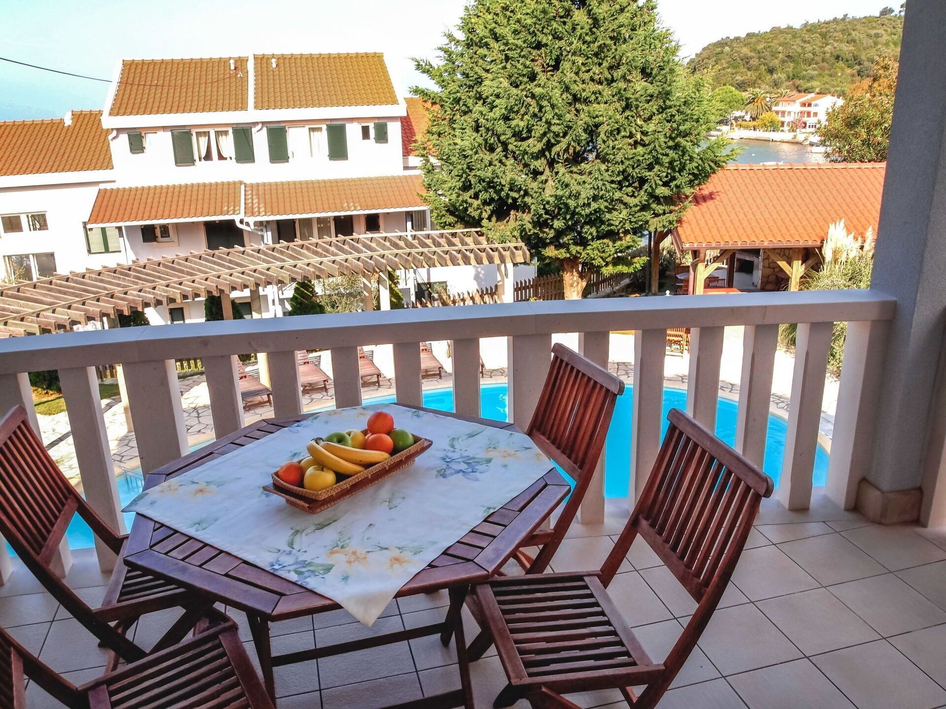 Un balcon avec une table dressée pour deux personnes, une piscine et des bâtiments en arrière-plan.