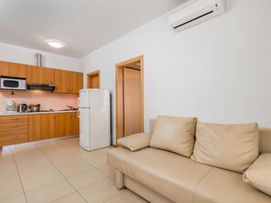 A compact living space with a kitchenette, a white refrigerator, a beige sofa, and a white air conditioner.