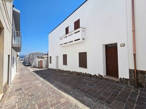 A narrow street with white buildings, stone paving, and a clear blue sky.