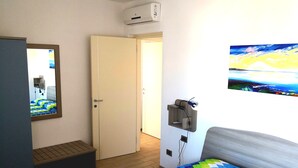 Een slaapkamer met een bed, een wandtelevisie, een deur en een klein plankje met een afstandsbediening.