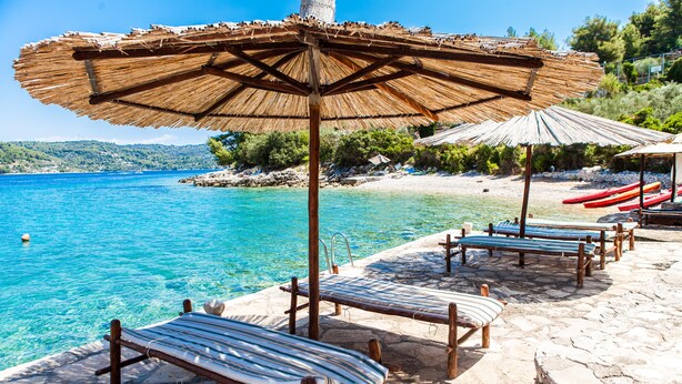 A beachside lounge with wooden loungers and thatched umbrellas, overlooking clear blue waters. - Sunny side Beach house (Vela Luka)