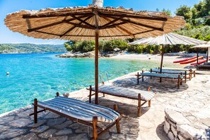 Un salon de plage doté de chaises longues en bois et de parasols en chaume, offrant une vue sur une eau d’un bleu cristallin.