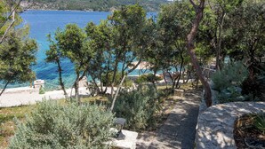 A coastal view with a stone pathway leading to a beach area with seating and a lamp post. - Sunny side Beach house (Vela Luka)