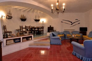 A spacious living room with a high ceiling, a chandelier, a dining area with wooden furniture, and a television.