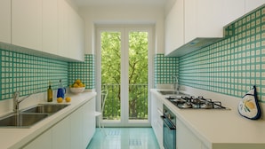 Una cocina moderna con armarios blancos, una estufa a gas y un lavamanos. Se ve un ventanal con vistas a árboles.
