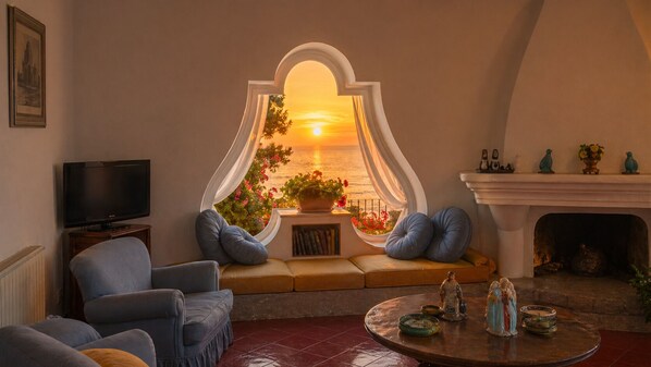 A living room with a television, seating, a fireplace, and a view of the sunset.