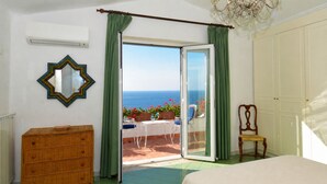 Un dormitorio con una cama grande, un aparador, una silla y vista al mar a través de una puerta corrediza de vidrio.