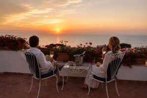 Two people seated at a table with a bottle of champagne, overlooking a sunset over the sea.