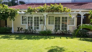 Um edifício com telhado de telhas vermelhas, janelas com moldura branca e varanda coberta.
