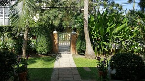 Caminho no jardim que leva a um portão, cercado por vegetação exuberante e plantas tropicais.