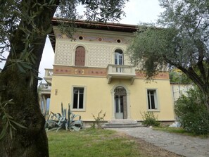 A two-story building with a yellow facade, a central entrance with a door, and a balcony on the upper floor.