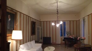 A room with striped wallpaper, a white sofa, a dining table with chairs, a chandelier, and a large window. - Splendid historic liberty villa (Malcesine)