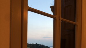 A view through a window with a door frame, overlooking a body of water, trees, and a distant shoreline. - Splendid historic liberty villa (Malcesine)