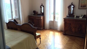 A bedroom with a bed, a wooden dresser, a mirror, and a door leading to a balcony. - Splendid historic liberty villa (Malcesine)