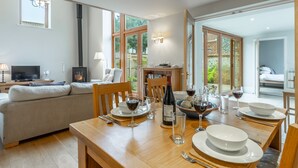 A modern living room with a dining area, featuring a sofa, wooden dining table, and a fireplace. - Palgrave Barn, Burnham Market, Norfolk (Burnham Market)