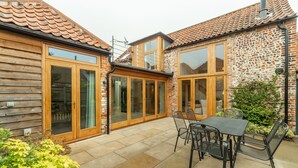 A patio with a table and chairs, a wooden fence, and a brick wall. - Palgrave Barn, Burnham Market, Norfolk (Burnham Market)