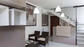 Un intérieur moderne avec un escalier, un coin repas doté de meubles en osier et un éclairage suspendu.