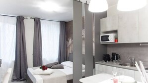 Une chambre d’hôtel moderne équipée d’un lit, d’une petite table avec un verre et d’une kitchenette.