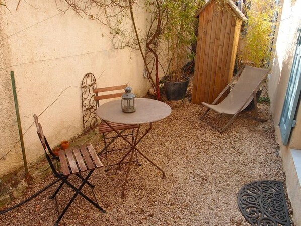 A small outdoor patio with a round table and two chairs, a lantern, a wooden fence, and a potted plant.